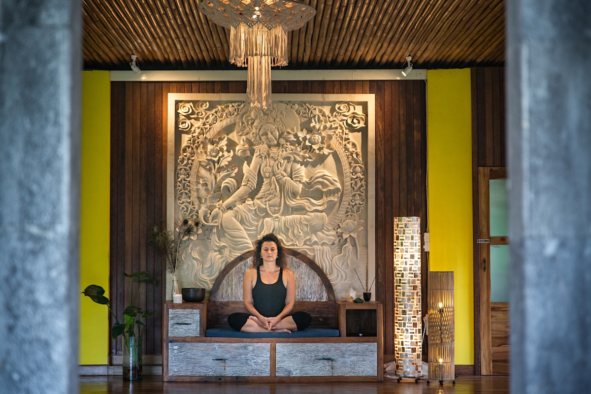 Woman meditating on wooden bench before stone Tara relief