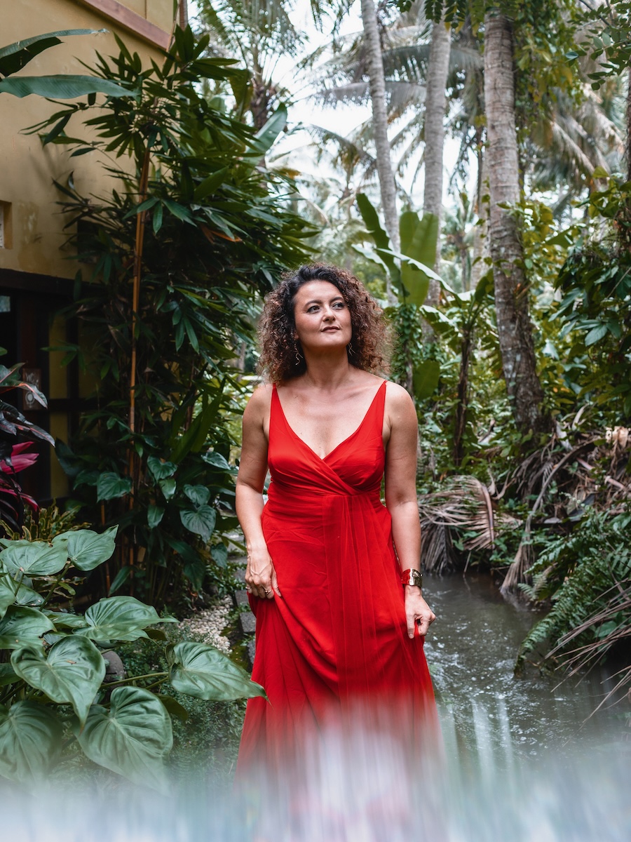 Dijan in red gown among tropical foliage beside a stream.