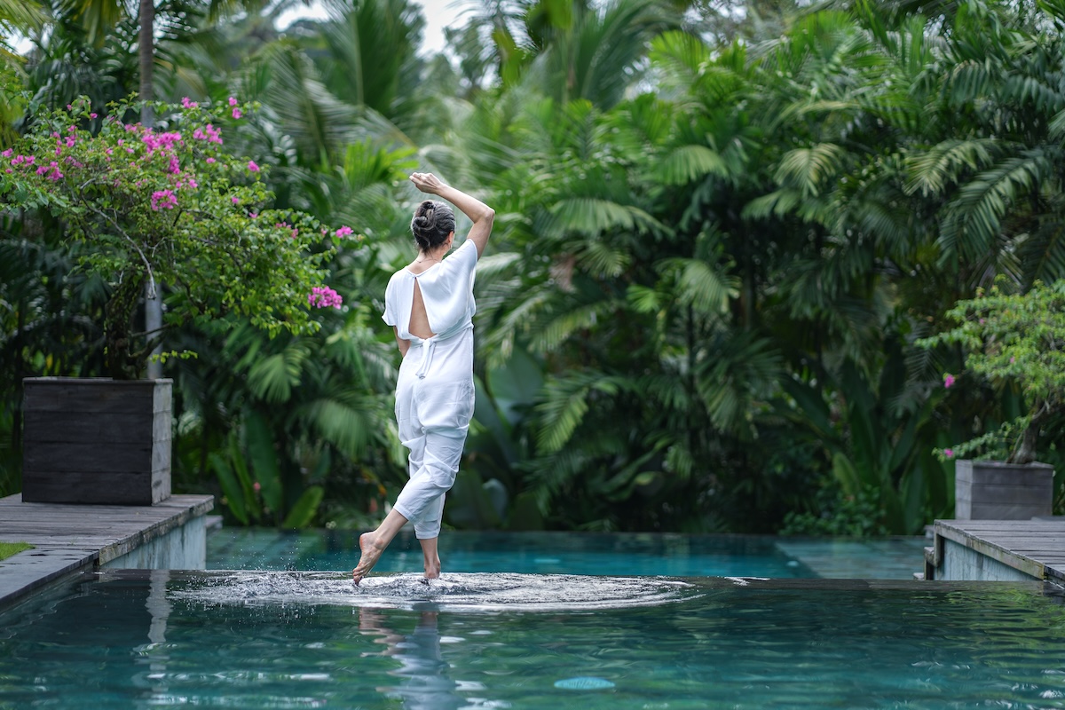 Woman in white stepping across an infinity pool surrounded by tropical greenery in Bali.