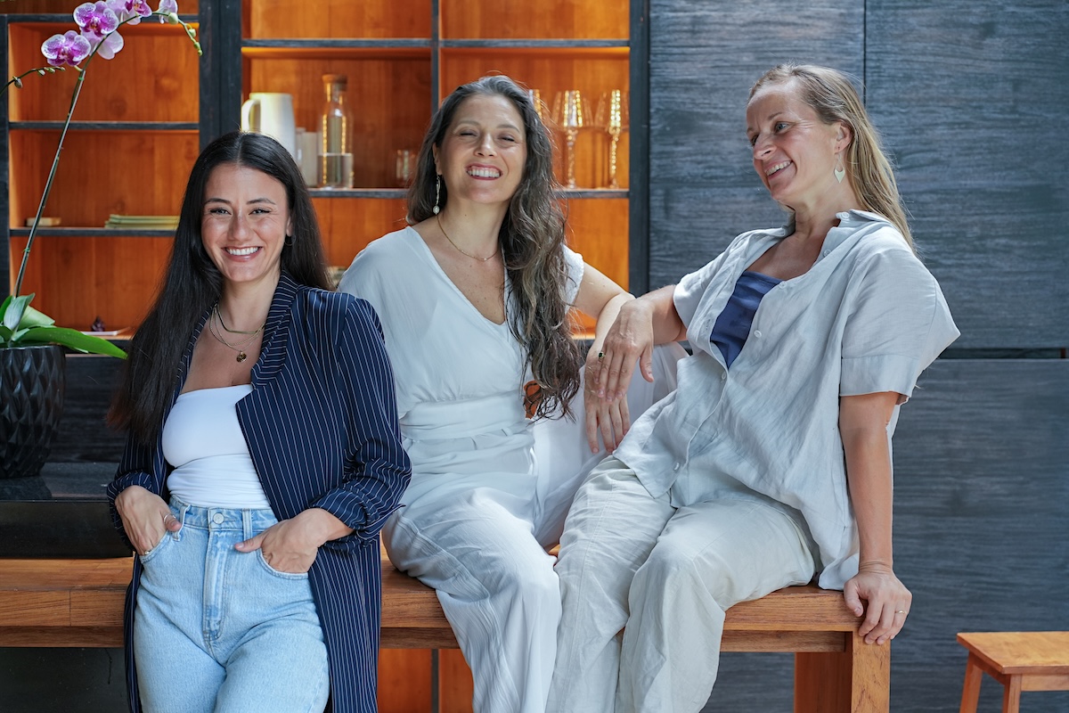 Three women laughing together on a bench