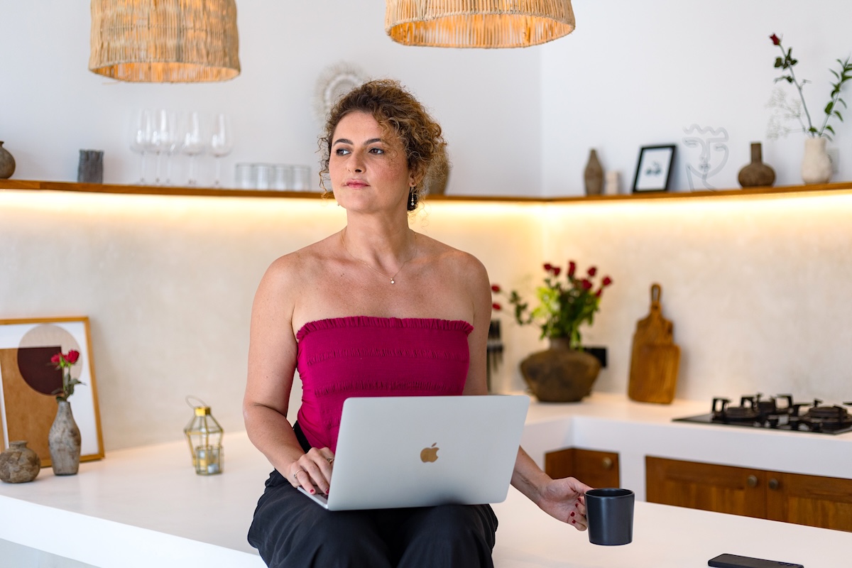 Dijan seated on her kitchen counter with a laptop and coffee cup, working from home.