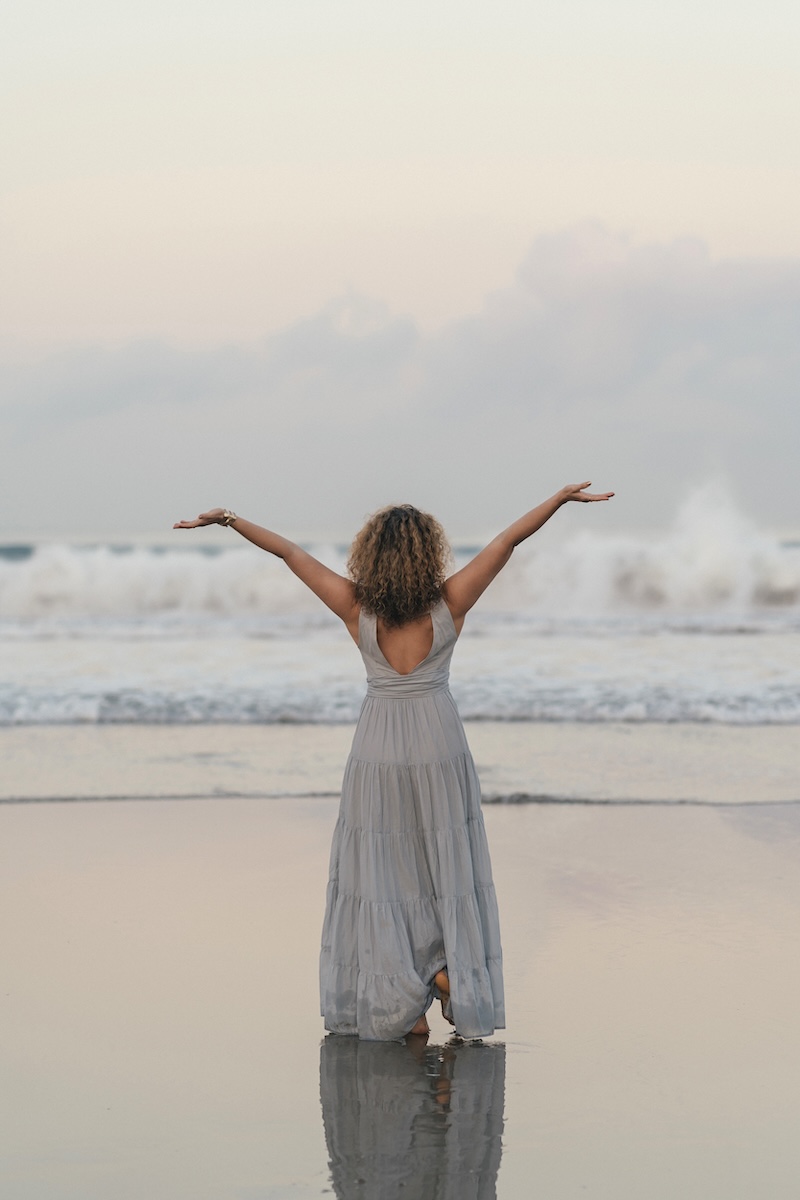 Dijan with arms open to the ocean at dusk