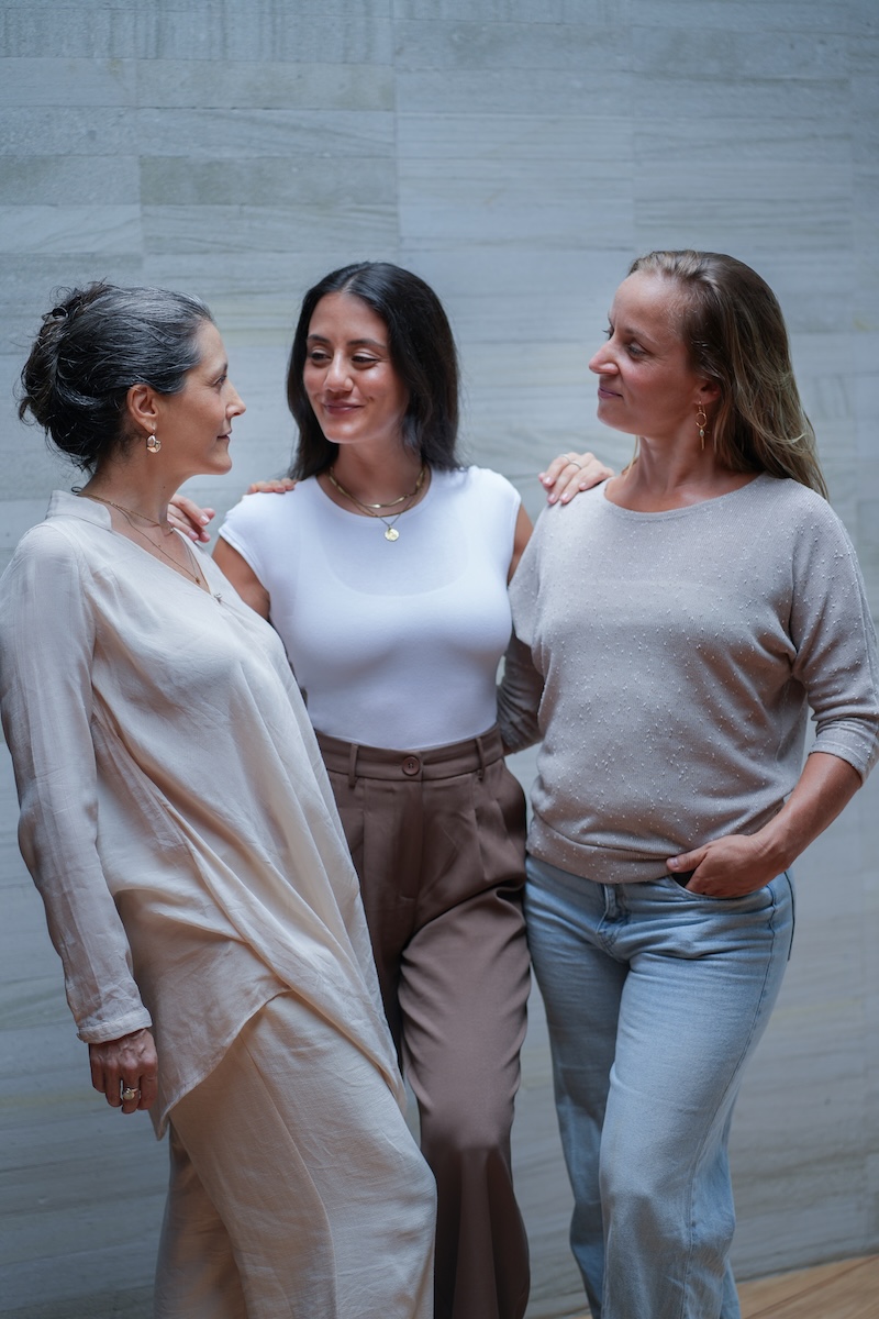 Three women of different ages standing together against stone wall