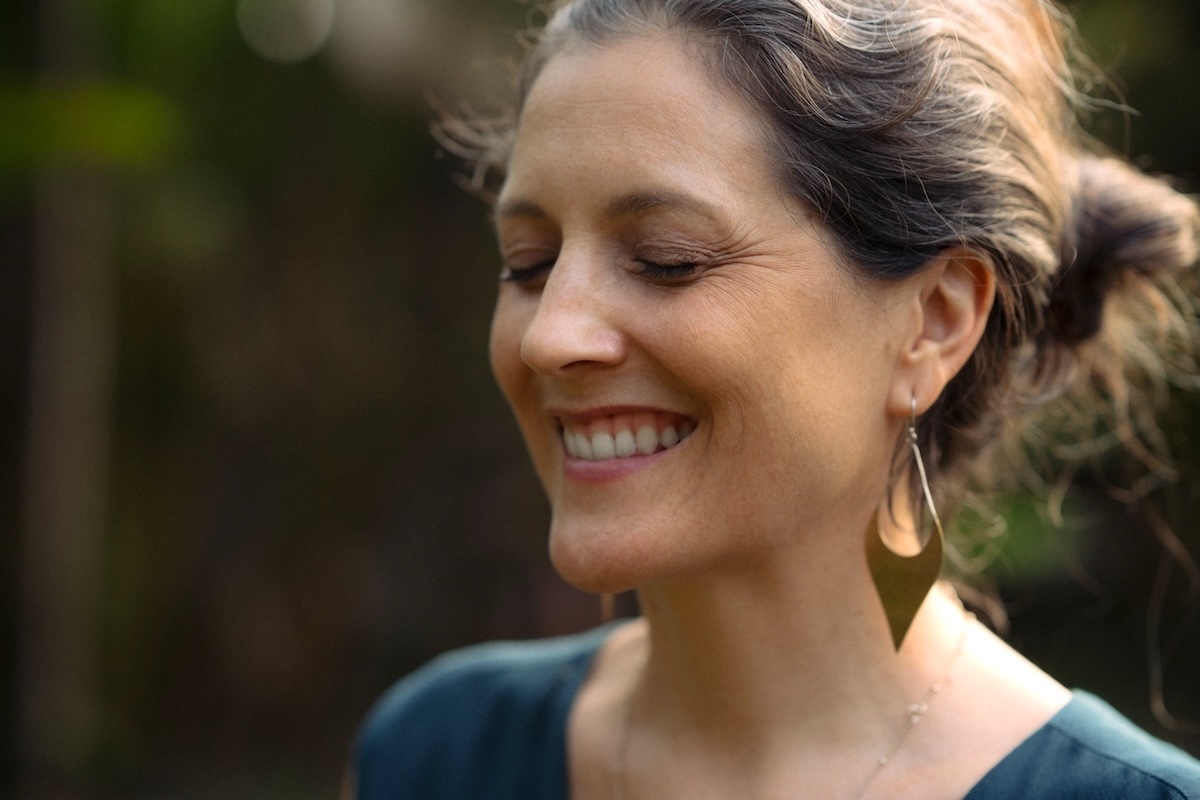 Close portrait of a woman smiling with eyes closed in soft daylight.
